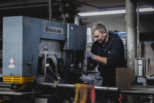 A metal worker clamps a piece of metal into a machine