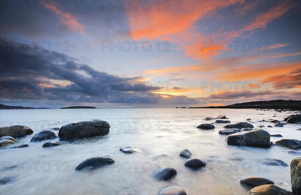 Orange coloured cloudy sky at sunset on a sandy beach strewn with round stones near Achiltibuie on the west coast of Scotland