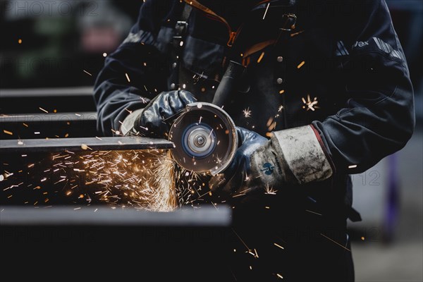 A metal worker works on a steel beam with a cut-off grinder