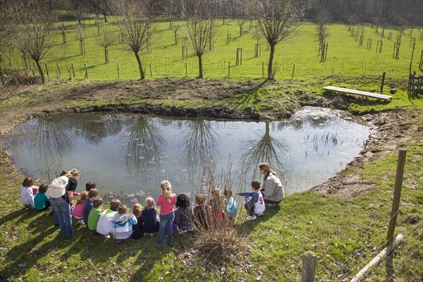 School children with teachers looking at frogspawn in old watering place for cattle