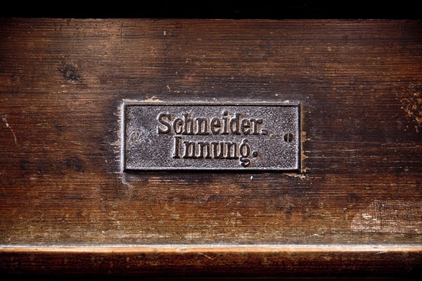 Permanently mounted sign of the tailors' guild on the church pew in the Nikolaikirche