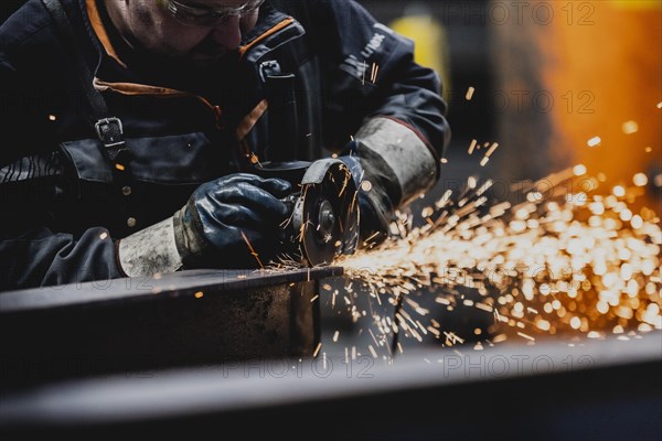 A metal worker works on a steel beam with a cut-off grinder