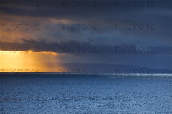 Evening sun breaks through low-lying rain clouds over the Summer Isles and the open waters of the blue Atlantic