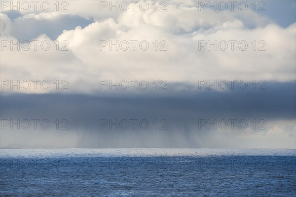 Low-lying rain clouds drift over the open waters of the blue Atlantic Ocean