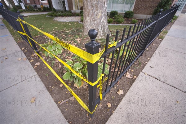 Yellow caution tape taking the place of a missing section in a metal fence