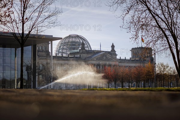 A water sprinkler waters a meadow in front of the Reichstag in the morning. Berlin