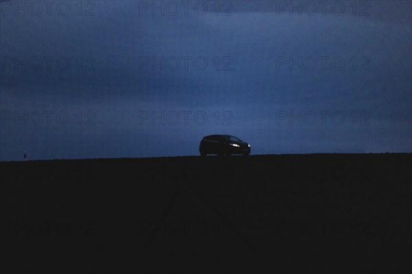 A car drives onto a country road at blue hour