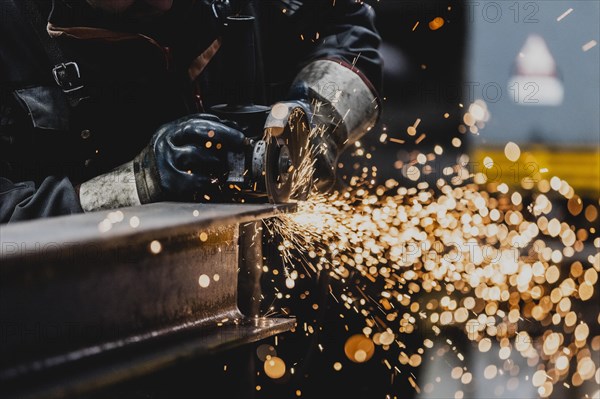 A metal worker works on a steel beam with a cut-off grinder