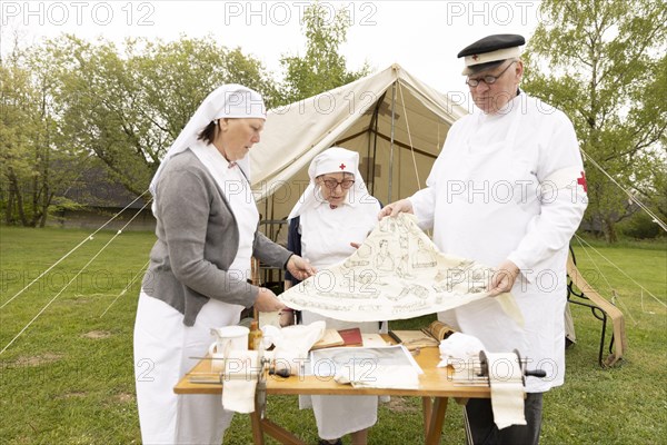 Red Cross volunteers present a bandage cloth in a historical outfit in front of a field hospital