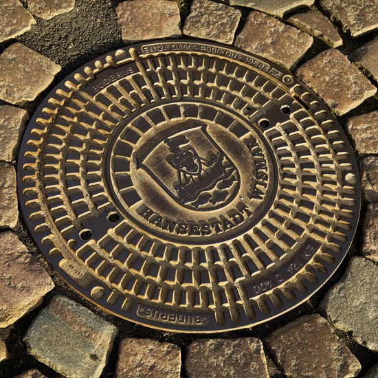 Manhole cover with city coat of arms and cobblestone pavement