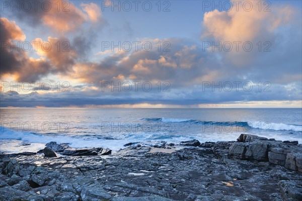 Low lying rain clouds drifting over the open waters of the blue Atlantic at sunset with orange coloured cloudy sky