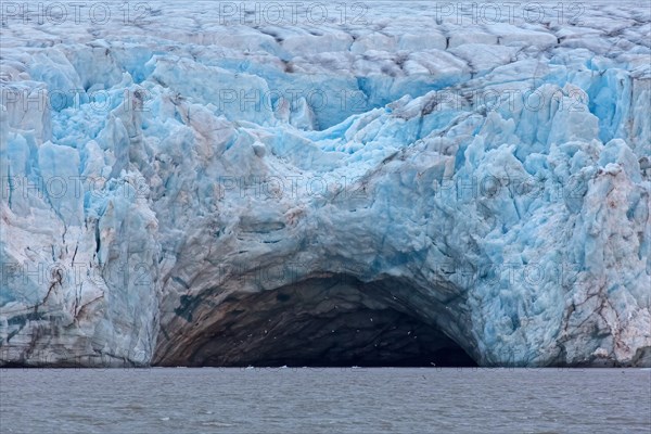 Seabirds flying at entrance of giant ice cave in the Kongsbreen glacier calving into Kongsfjorden