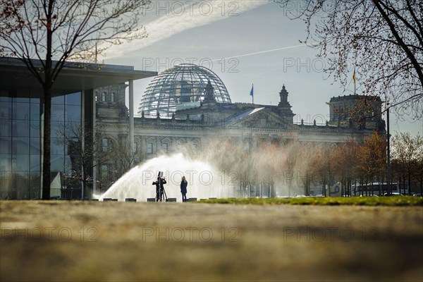 A water sprinkler waters a meadow in front of the Reichstag in the morning. Berlin