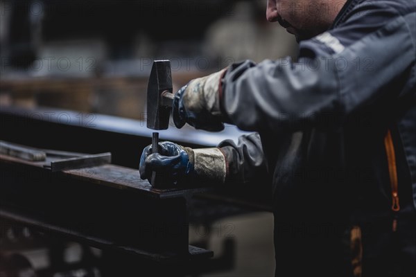 A metal worker marks a drill hole on a steel beam