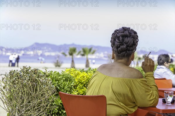 Woman with a striking hairstyle sitting in a beach cafe smoking