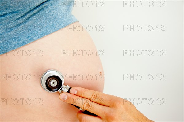 A doctor holding a stethoscope to a pregnat woman's belly