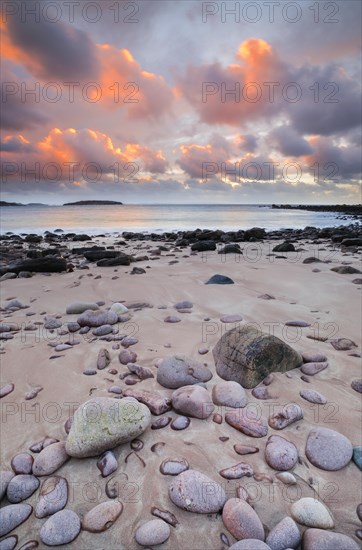 Orange coloured cloudy sky at sunset on a sandy beach strewn with round stones near Achiltibuie on the west coast of Scotland
