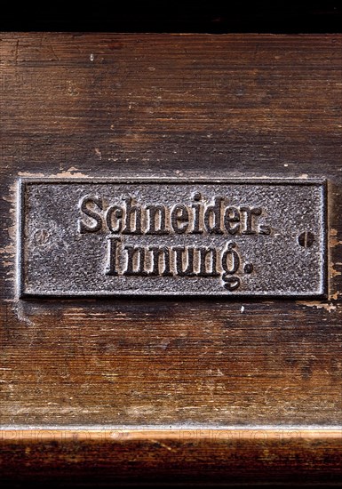 Permanently mounted sign of the tailors' guild on the church pew in the Nikolaikirche