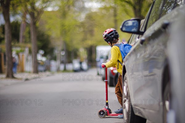 Symbolic photo on the subject of children in road traffic A little boy stands with his scooter between parked cars on a street. Berlin