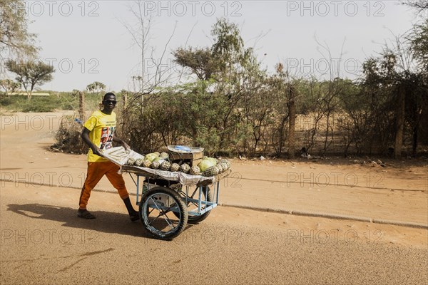 A street vendor with pineapples walks along a street