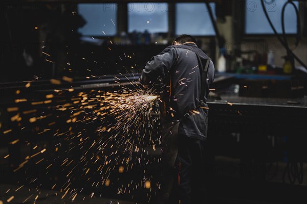 A metal worker works on a steel beam with a cut-off grinder