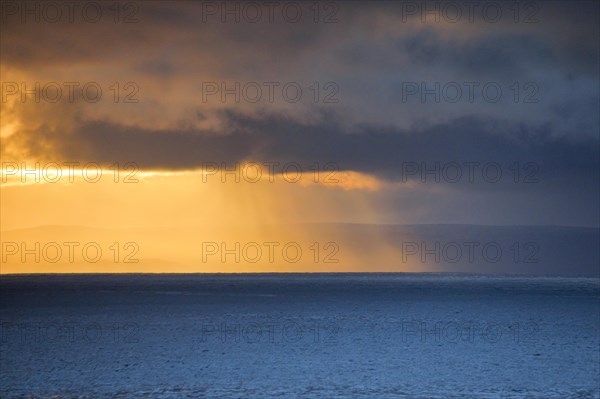 Evening sun breaks through low-lying rain clouds over the Summer Isles and the open waters of the blue Atlantic