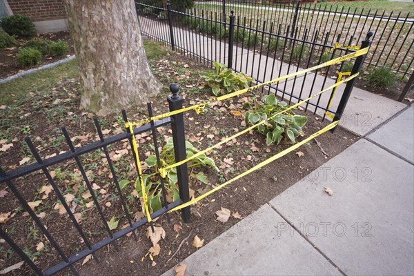 Yellow caution tape taking the place of a missing section in a metal fence