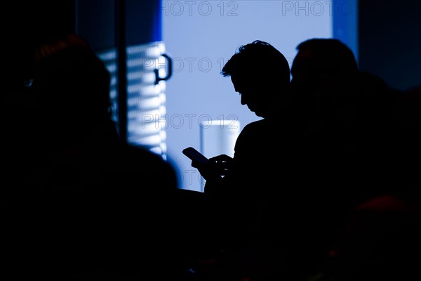 A man sits in the audience of an event and types on his smartphone. Berlin