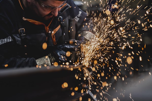 A metal worker works on a steel beam with a cut-off grinder