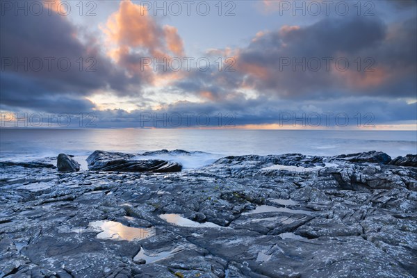 Low lying rain clouds drifting over the open waters of the blue Atlantic at sunset with orange coloured cloudy sky