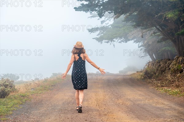 A tourist woman walking through the foggy path towards the juniper forest in El Hierro. Canary Islands