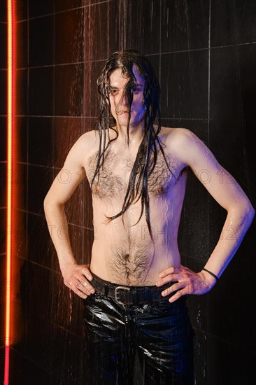 Handsome young man with long hair and wet torso on a dark background in shower