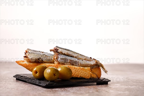 Tapa of sardines with tomato and olives on black slate and white background typical Spanish