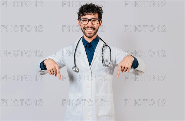 Young doctor pointing a promotion down. Handsome doctor pointing down an isolated advertising space. Happy doctor pointing fingers down