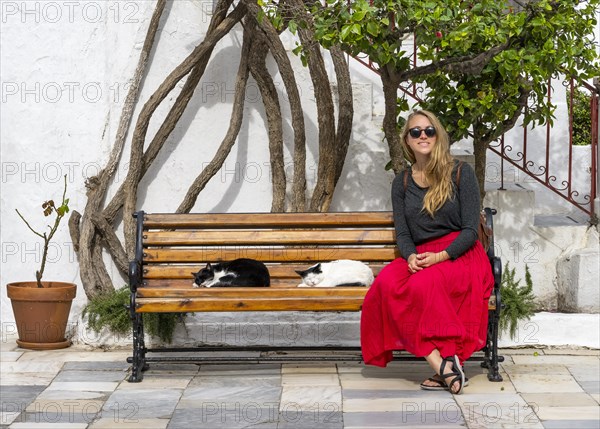 Young woman with red skirt sitting on a bench with sleeping cats
