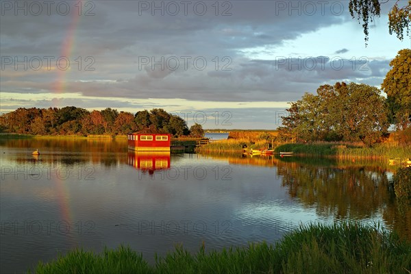 Red wooden house and trees reflected in calm water