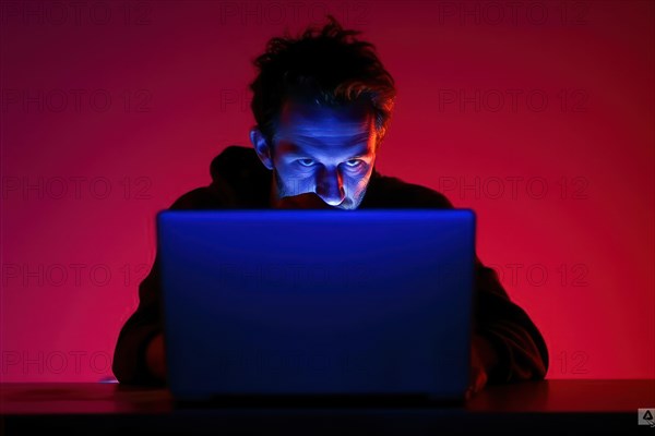 A man in his early 40s works at his laptop at night