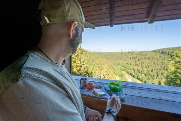 Man with cap takes a break and eats Vesper on the Fautsburg with view of the Black Forest