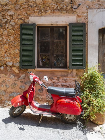 Red Vespa in front of the window of a typical stone house