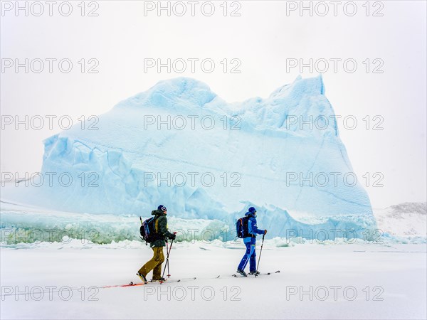 Ski tourers in front of iceberg in frozen Kong Oscar Fjord