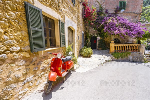 Red Vespa in front of the window of a typical stone house