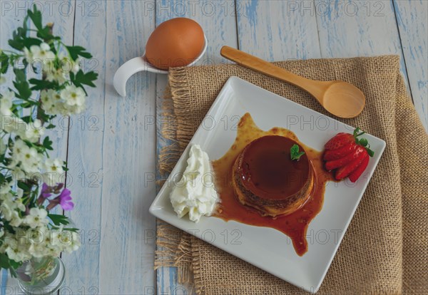 Egg custard with cream and strawberries on a white plate on a blue wooden table with flowers