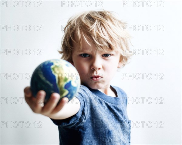 A five-year-old blond boy with an angry look demonstratively stretches out his arm with a globe in his hand