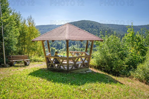 Woman eating pretzel in wooden pavilion and looking at the endless forest on the hiking trail Sprollenhaeuser Hut