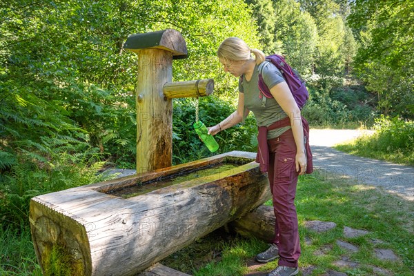 Hiking woman fills drinking bottle at the wooden fountain on the hiking trail Sprollenhaeuser Hut