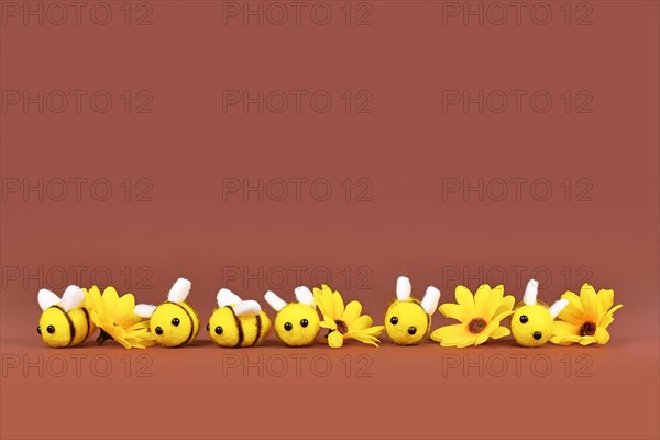 Felt bees and yellow flowers in a row on brown background with copy space