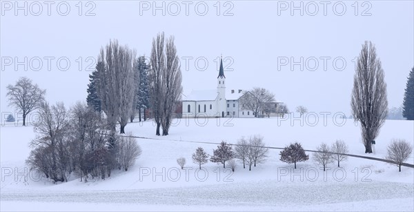 Small hamlet with chapel in snowy landscape in gloomy winter weather