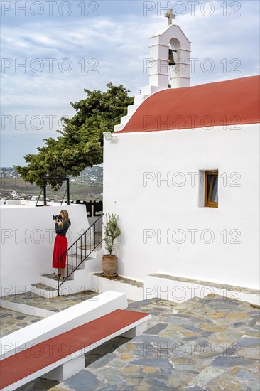 Young woman with red skirt photographed at a Cycladic white and red Orthodox church