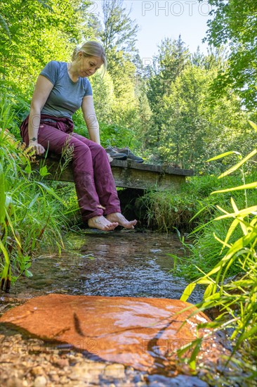 Woman sitting by stream holding feet in water on hiking trail Sprollenhaeuser Hut