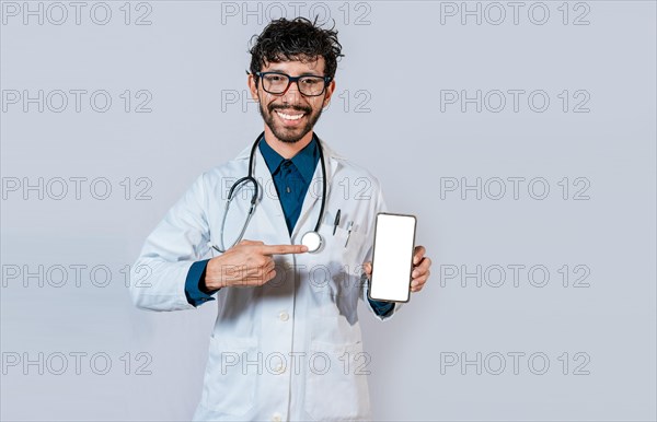 Smiling doctor holding and pointing at cell phone screen. Young doctor showing and pointing at smatphone screen isolated